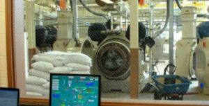 A computer screen shows the operation conditions of a pellet mill shown in the distance