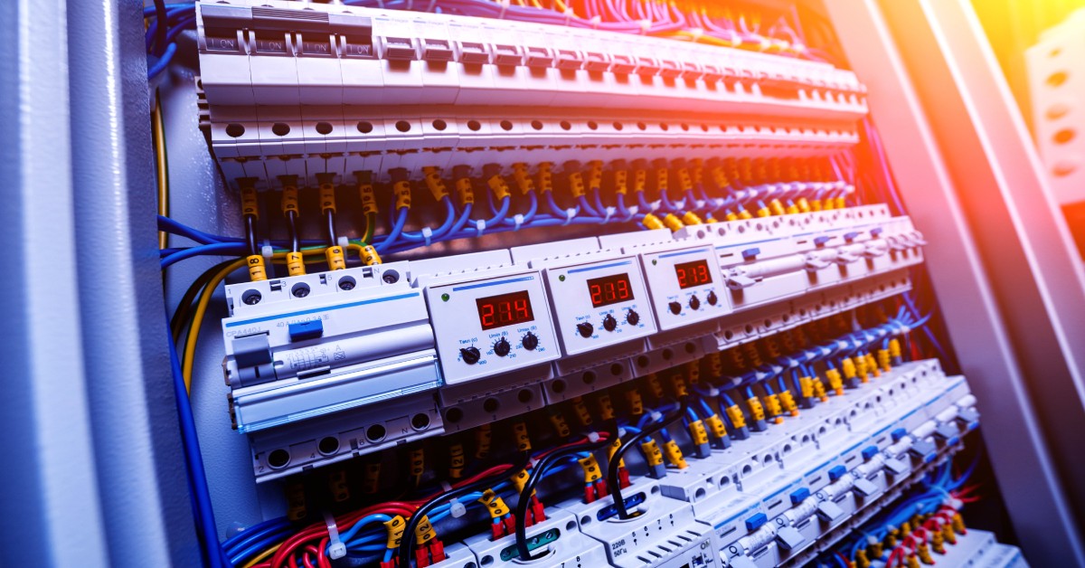 A close-up of a large electric control panel with multiple rows of circuit breakers, cables, screens, and meters.