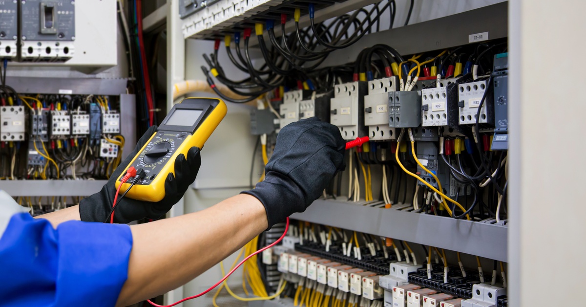 Person wearing a blue uniform and protective black gloves measuring the power of an electric control system.
