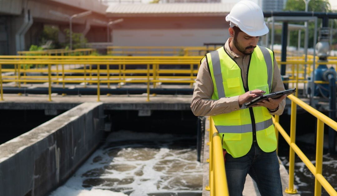 A worker holding a tablet while standing on a bridge on top of a large concrete container with dark water.